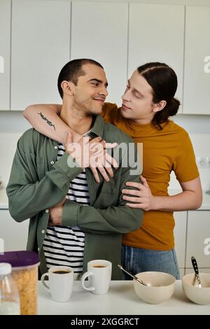 Un jeune couple gay s’embrasse dans leur cuisine moderne, mettant en valeur leur amour et leur intimité. Banque D'Images