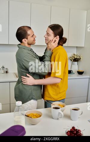 Un jeune couple gay partage un moment tendre dans leur cuisine moderne, leur tenue décontractée et leur posture détendue suggérant une atmosphère chaleureuse et intime. Banque D'Images