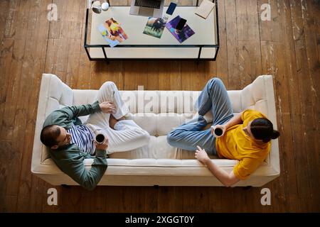 Un jeune couple gay se détend sur un canapé blanc dans leur appartement moderne, dégustant un café ensemble. Banque D'Images