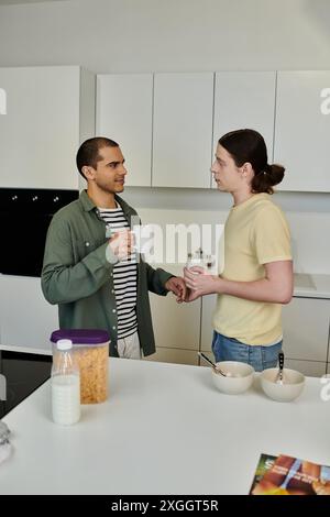 Un jeune couple gay profite d'une matinée détendue ensemble dans leur appartement moderne, partageant une tasse de café et un petit déjeuner léger. Banque D'Images