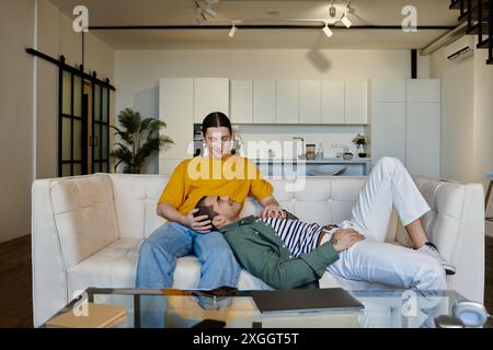 Un jeune couple gay se détend sur un canapé blanc dans leur appartement moderne. Banque D'Images