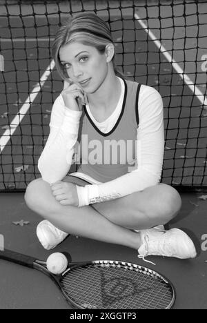 Caucasian Teen Girl in Tennis Outfit penché contre Net avec raquette et balle. ÉTATS-UNIS Banque D'Images