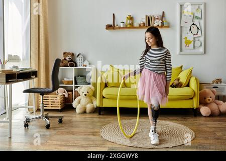 Une jeune fille avec une jambe prothétique fait tourner un hula hoop jaune dans son salon, entourée de jouets et d'un canapé jaune. Banque D'Images