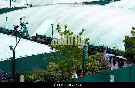 Une vue générale des courts extérieurs couverts et des spectateurs abrités sous des parapluies de la pluie le neuvième jour des Championnats de Wimbledon 2024 au All England Lawn Tennis and Croquet Club, Londres. Date de la photo : mardi 9 juillet 2024. Banque D'Images