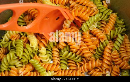 Pâtes Rotini trois couleurs. Fond tricolore de pâtes fusilli. Texture abstraite de pâtes colorées. Motif de macaronis. Nourriture multicolore lumineuse. Banque D'Images