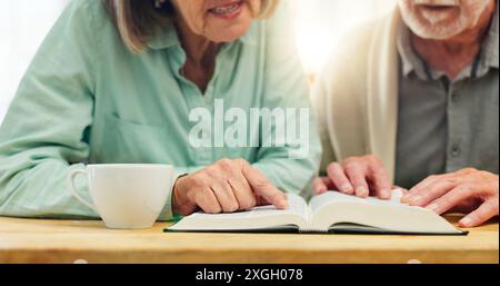 Bible, mains et lecture avec couple senior buvant du thé à table dans l'appartement ensemble pour la croyance ou la foi. Livre, Jésus ou Dieu avec homme et femme dedans Banque D'Images