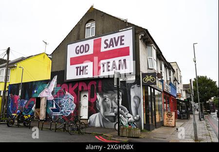 Brighton Royaume-Uni 9 juillet 2024 - Un panneau géant God Save the Team par l'artiste Corbyn Shaw juste à côté de Lewes Road à Brighton la veille de l'affrontement de l'Angleterre contre les pays-Bas dans leur match de demi-finale à l'Euro 2024 en Allemagne . Il fait partie de Buildhollywood qui se spécialise dans l'art créatif de la publicité de rue dans les villes britanniques : crédit Simon Dack / Alamy Live News Banque D'Images