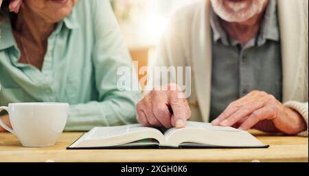 Bible, mains et étude avec couple senior buvant du thé à table dans l'appartement ensemble pour la croyance ou la foi. Livre, Jésus ou Dieu avec l'homme et la femme Banque D'Images