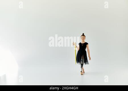 Une jeune fille avec une jambe prothétique pratique la gymnastique avec un cerceau jaune dans un studio blanc. Banque D'Images