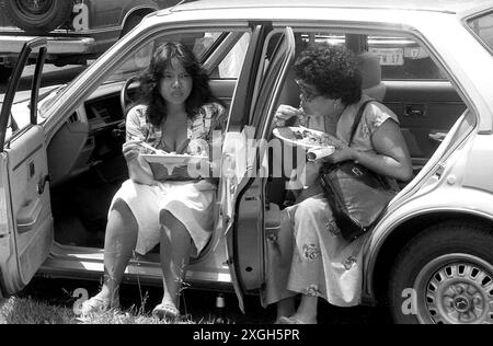 Maryland, États-Unis, 1982. Photo franche de deux femmes Philippines mangeant dehors en s'asseyant dans le véhicule. Banque D'Images