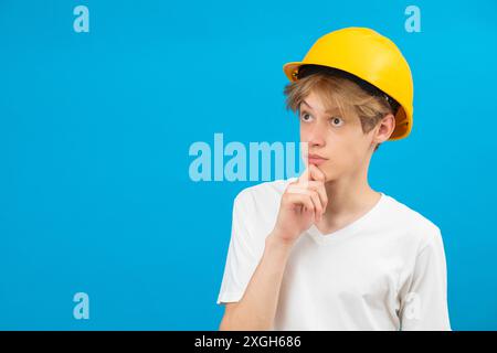 Portrait d'intérieur d'un bel artisan debout isolé sur fond bleu, regardant directement la caméra avec un casque jaune sur la tête. People et WO Banque D'Images