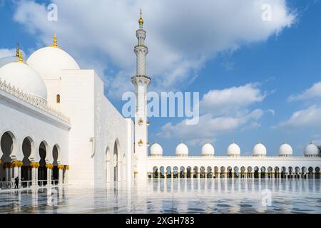 Abu Dhabi, Émirats arabes Unis – 4 janvier 2024 : arches élégantes et bassins réfléchissants à la sereine Grande Mosquée Sheikh Zayed sous un ciel bleu. Banque D'Images