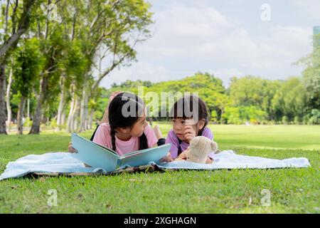 Deux enfants s'allongent et lisent un livre dans le jardin de jeunes filles sœurs allongées dans le parc et lisant un livre par une chaude journée d'été. Belle asiatique Banque D'Images