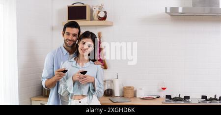 Heureux couple tient un verre de vin à leurs fronts appréciant. Date romantique debout dans la cuisine moderne à la maison ensemble femme souriante et mari celebr Banque D'Images