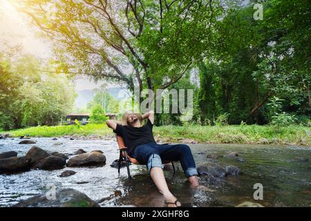 L'homme barbu mature est assis sur une chaise au milieu du ruisseau et écrit joyeusement le week-end, les visages souriants se réjouissent dans le reste. Banque D'Images