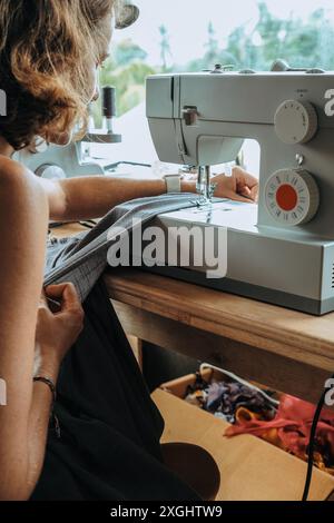 Vue arrière d'une jeune femme tailleur qui s'assoit à une machine à coudre et coud Banque D'Images