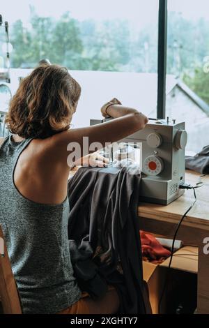 Vue arrière d'une jeune femme tailleur qui s'assoit à une machine à coudre et coud Banque D'Images