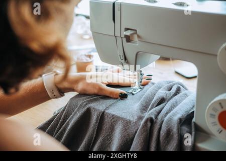 Vue arrière d'une couturière femme qui s'assoit à une machine à coudre et coud Banque D'Images