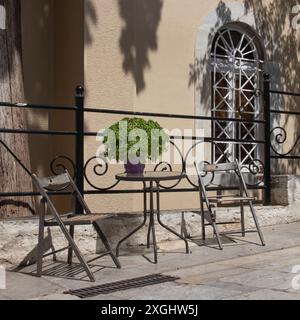 Deux vieilles chaises de cadre en métal et une table avec pot de plante sur le trottoir Athènes Grèce fournissent un endroit pour se reposer de la chaleur Banque D'Images