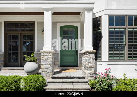 Un détail de porte d'entrée sur une maison de ferme moderne blanche avec une porte d'entrée verte et un porche couvert avec un sol en pierre et des piliers. Aucune marque ou étiquette. Banque D'Images