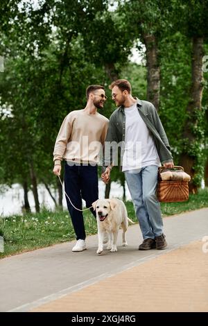 Un couple gay barbu profite d'un pique-nique dans un parc verdoyant avec son chien labrador. Banque D'Images