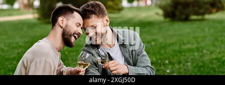 Un couple gay barbu profite d'un pique-nique dans un parc verdoyant tout en partageant un rire et un verre de vin. Banque D'Images