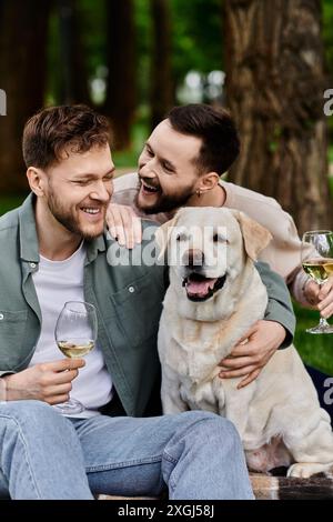 Un couple gay barbu rit avec leur chien labrador tout en profitant d’un pique-nique dans un parc verdoyant. Banque D'Images