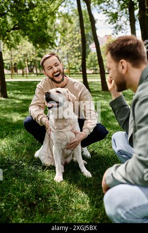 Un couple gay avec la barbe rit tout en passant du temps avec leur labrador dans un parc verdoyant. Banque D'Images