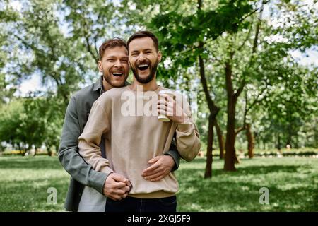 Un couple gay barbu en tenue décontractée rit et embrasse tout en passant du temps ensemble dans un parc verdoyant. Banque D'Images