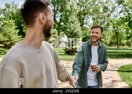 Un couple gay barbu se promène main dans la main dans un parc verdoyant, riant et profitant de la compagnie de l'autre. Banque D'Images