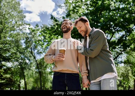 Un couple gay barbu partage un rire en marchant dans un parc par une journée ensoleillée. Banque D'Images