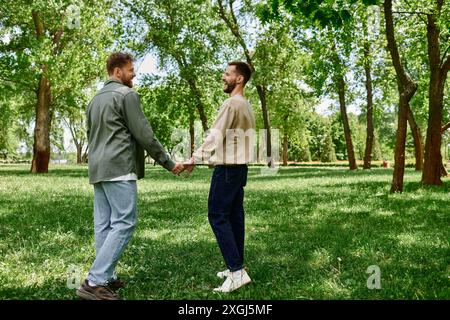 Un couple gay barbu se promène main dans la main dans un parc verdoyant, souriant et appréciant les uns les autres en compagnie. Banque D'Images