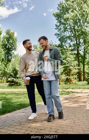 Un couple gay barbu marche main dans la main à travers un parc verdoyant luxuriant, riant et appréciant les uns les autres en compagnie. Banque D'Images