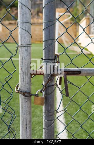 Gros plan d'une porte verrouillée avec une chaîne et un cadenas sur un terrain de football. Symbolise la sécurité, les restrictions et les limitations. Banque D'Images