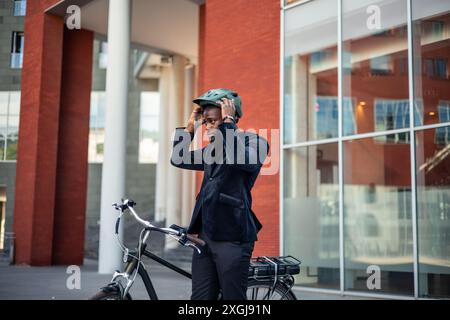 Un homme d'affaires afro-américain noir est vu mettre son casque, se préparer à se rendre au travail sur son vélo électrique, mettant l'accent sur le transp durable Banque D'Images