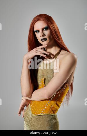 Une drag queen dans une robe à paillettes dorées et un maquillage étincelant pose dans un studio. Banque D'Images