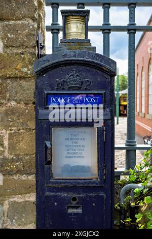 Une vieille boîte téléphonique bleue de la police stationnée contre un mur de briques avec une ambiance historique. Banque D'Images