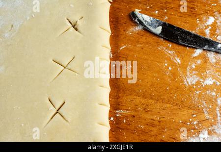 Faire une tarte : croûte supérieure. Une fois la croûte supérieure déroulée, elle est pliée et un couteau est utilisé pour créer des trous d'aération dans la pâte. Banque D'Images