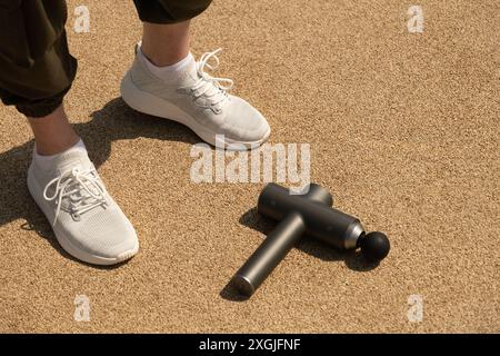Jambes d'athlète et masseur à percussion pour réchauffer les muscles de la jambe avec un masseur à impact sur la zone de sport en plein air. Concept. Banque D'Images