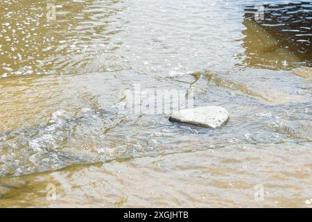 L'eau coule autour d'une pierre avec une surface lisse. Promenez-vous dans le parc. Banque D'Images