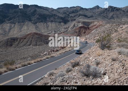 Deux voitures roulent sur une route dans le désert. La route est sinueuse et les voitures roulent à une vitesse lente. Le paysage désertique est rocheux et aride, wi Banque D'Images