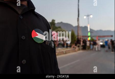 Un musulman chiite du Cachemire portant une broche de drapeau palestinien sur son t-shirt, avec d'autres, érige un grand drapeau religieux sur une route pendant Mouharram. Mouharram a commencé au Cachemire avec une profonde révérence, en particulier parmi la communauté musulmane chiite, commémorant le martyre de l'imam Hussain lors de la bataille de Karbala. Les dix premiers jours, culminant à Ashura, comportent des processions solennelles où les personnes en deuil vêtues de bannières noires portent des bannières et effectuent des battements rythmés de poitrine. Les rassemblements de Majlis ont lieu où les érudits religieux racontent les événements de Karbala, et les récitations émotionnelles de Marsiya sont courantes. Intric Banque D'Images