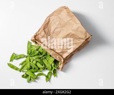 'Vue de dessus de pois mange-tout frais débordant d'un sac en papier brun, sur fond blanc propre. Idéal pour la cuisine, le jardinage et la santé Banque D'Images