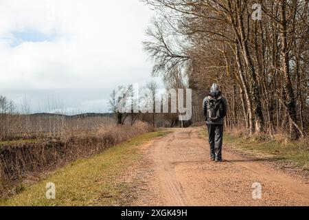 Un garçon marche le long d'un chemin solitaire dans un paysage d'automne. Il porte un sac à dos et la capuche vers le haut. Banque D'Images