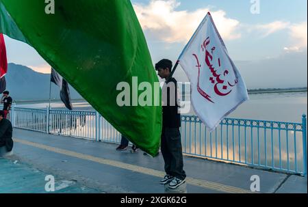 Un garçon musulman chiite du Cachemire tient un drapeau religieux alors qu'il regarde un grand drapeau religieux installé sur une route pendant Mouharram. Mouharram a commencé au Cachemire avec une profonde révérence, en particulier parmi la communauté musulmane chiite, commémorant le martyre de l'imam Hussain lors de la bataille de Karbala. Les dix premiers jours, culminant à Ashura, comportent des processions solennelles où les personnes en deuil vêtues de bannières noires portent des bannières et effectuent des battements rythmés de poitrine. Les rassemblements de Majlis ont lieu où les érudits religieux racontent les événements de Karbala, et les récitations émotionnelles de Marsiya sont courantes. Taziy finement conçu Banque D'Images