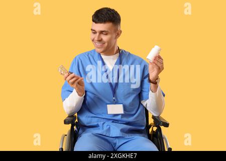 Jeune médecin masculin en fauteuil roulant avec des pilules sur fond jaune Banque D'Images