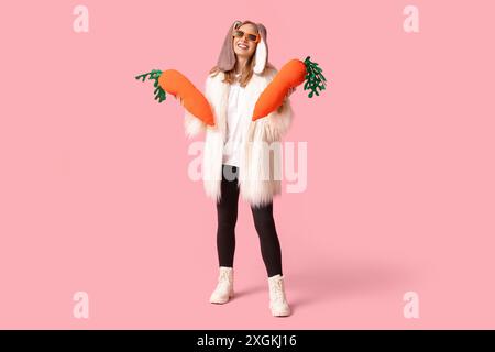 Belle femme dans les oreilles de lapin avec des carottes en jouet sur fond rose. Fête de Pâques Banque D'Images