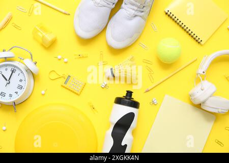Réveil, écouteurs, volant, Frisbee, bouteille d'eau sportive, balle de tennis et papeterie différente sur fond jaune Banque D'Images