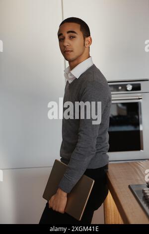 Jeune professionnel travaille à distance dans une cuisine moderne, exsudant confiance et détente. Cette image capture l'essence d'un entrepreneur millénaire Banque D'Images