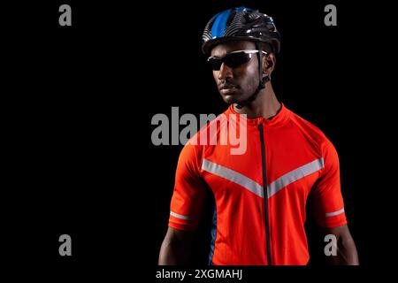 Cycliste afro-américain pose en toute confiance sur fond noir, avec espace de copie. Sa tenue sportive et son casque suggèrent un accent sur la sécurité routière et PER Banque D'Images